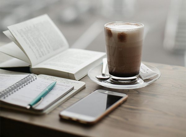 A coffee, notebook, and phone on a wooden desk